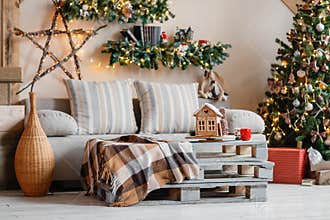 Calm image of interior modern home living room decorated christmas tree and gifts, sofa, table covered with blanket.