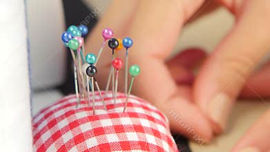 Anonymous woman puts down her scissors in front of a sewing machine and takes a needle or pin from her pincushion.