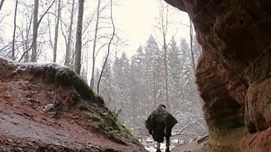 Prehistoric caveman goes outside from his cave on a background of winter forest