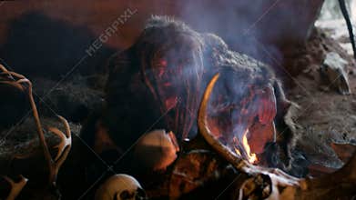 Phrehistoric cave man makes first fire, blows on it in his cave on the background of bones and skulls. Snow winter