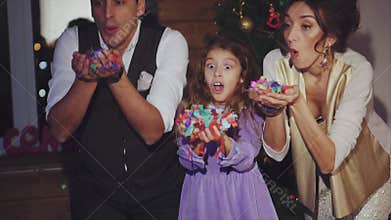Happy mom, dad and daughter blowing colorful confetti celebration of Christmas