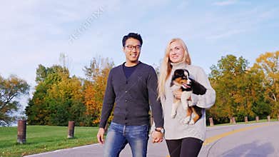 Happy Together with his beloved dog. Multiethnic couple walking in the park with his dog. Caucasian woman carries a