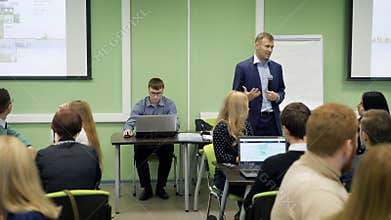 Lecturer in classroom at the university speaking the lecture for group of students. Speaker in blue suit with the