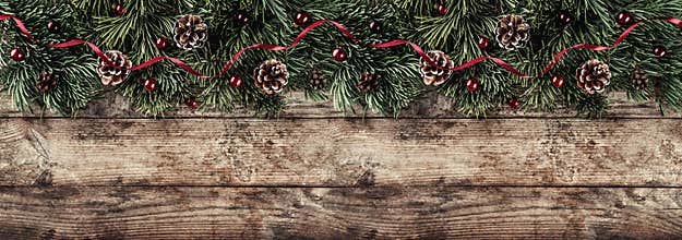 Creative layout frame made of Christmas fir branches, pine cones and red decoration on wooden background. Xmas and New Year theme.