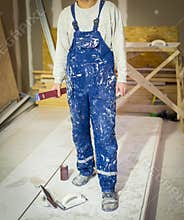 Worker in dirty uniform or boilersuit with water level and palette-knife in his hands in the room of apartment that is under