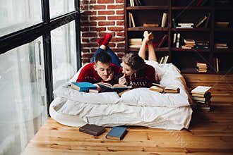 Couple in red Christmas sweater reading books on mattress at hom