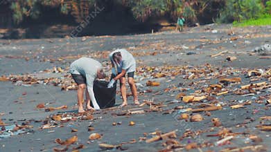 Group of volunteers cleaning up beach. The volunteer raises and throws a plastic trash into the bag. Environmental
