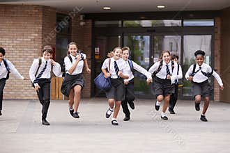 Group Of High School Students Wearing Uniform Running Out Of School Buildings Towards Camera At The End Of Class