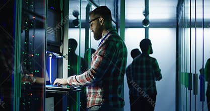 Bearded IT engineer using laptop in server room
