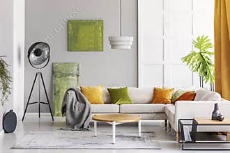 Paintings on the wall and industrial lamp in the corner of elegant living room interior with golden lime accents, real photo with