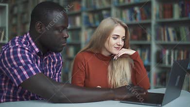 European lady and African American are laughing while working with a laptop