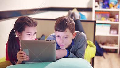 Little boy and girl are playing and dog on the tablet lying on the bed. boy and girl teens social media internet on a