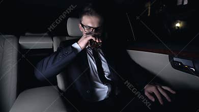 Millionaire drinking glass of elite brandy on back seat of car, business trip