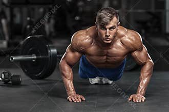 Muscular man working out in gym doing push-ups exercises, strong male naked torso abs