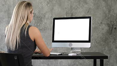 Young business woman working in office interior on pc on desk, typing, looking at screen. White Display.