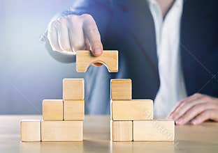 Business man bridging the gap between two towers or parties made from wooden blocks; conflict management or mediator concept