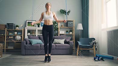 Slender girl in leggings and top jumping rope at home concentrated on activity