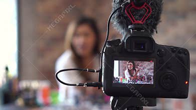 Asian woman recording video about cosmetics with DSLR on tripod