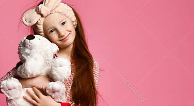 Smiling baby girl holding a white teddy bear in the room a pink backdrop.