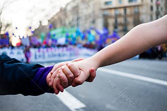 Young women holding hands during woman`s day rally with purple balloons in background for women rights and feminism