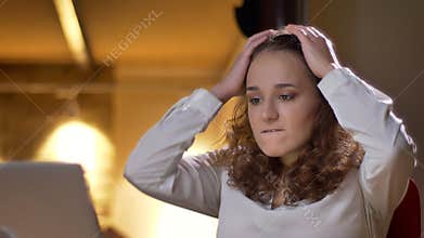 Portrait of concentrated young businesswoman watching into laptop with despair on office background.
