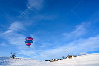 Hot-air balloon over snow covered landscape and small rural village, Bavaria, Germany