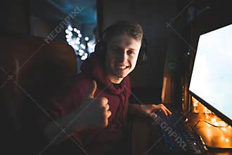 Happy young man playing games on a computer, sitting at home in a cemetery, looking into the camera