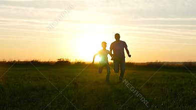 Happy family father and son running across the green field against the sunset background