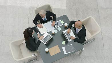 Three corporate business people meeting in office using laptop computers
