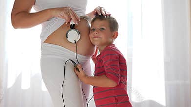 Child with android in hands puts earphones on belly of pregnant woman and baby in belly listens to music