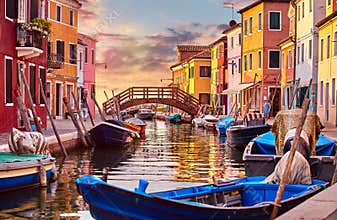 Burano island in Venice Italy picturesque sunset over canal with boats among old colourful houses stone streets.