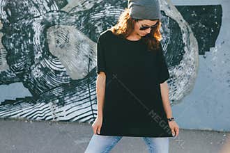Model wearing plain tshirt and sunglasses posing over street wall