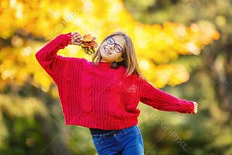 Happy fall girl smiling and joyful holding autumn leaves. Beautiful young girl with maple leaves in red cardigan