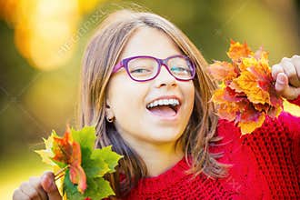 Happy fall girl smiling and joyful holding autumn leaves. Beautiful young girl with maple leaves in red cardigan