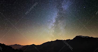 Scenic meteor explosion with stardust during time lapse of the Milky Way and the starry sky rotating over the Alps.
