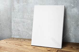 Blank white canvas frame leaning at concrete wall and wood floor