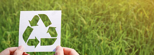 Cut paper with the logo of recycling over green grass