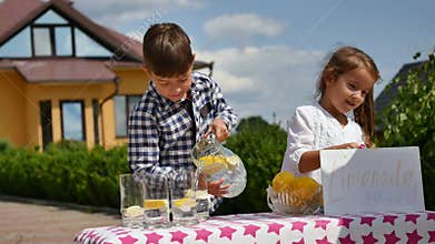 Two little kids are selling lemonade at a homemade lemonade stand on a sunny day with a price sign for an entrepreneur