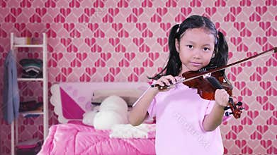 Adorable girl playing a violin in bedroom