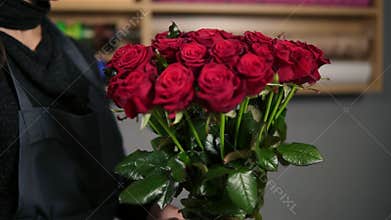 Focus on the bunch of red roses: young attractive female florist arranging bouquet of beautiful red roses at flower shop