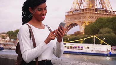 Young woman standing on embankment in Paris and watching photos on smartphone