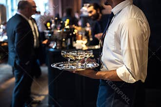 Waiter from catering service carrying champagne wine drinks on the event.