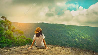 Young traveling woman wearing hat and sitting on the top of the mountain cliff with relaxing mood. Asian woman travel alone.