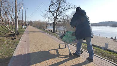 Back view of homeless man pushing shopping cart