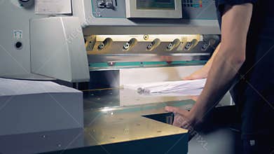 Printing house worker operating cutting machine. Worker cutting a stack of paper in a typography.