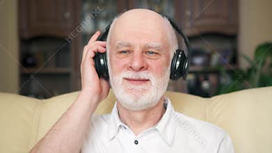 Modern senior man listening music with wireless headphones. Pensioner meloman dancing to music