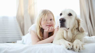 Life of domestic pets in the family. a small blonde girl lies with her dog on the bed in the bedroom. a golden retriever