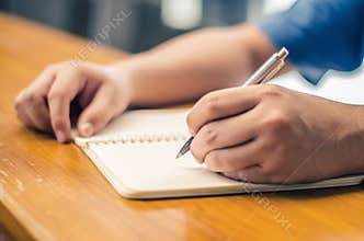 Close up of student hand writing on book with pen
