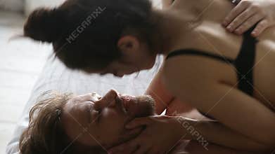 Playful young woman on top kissing boyfriend in bed, closeup