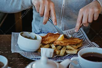 Man sitting at the wooden table, eating fish and chips.